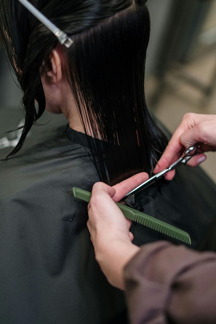 Hairdresser cutting wet, dark hair with scissors and comb.