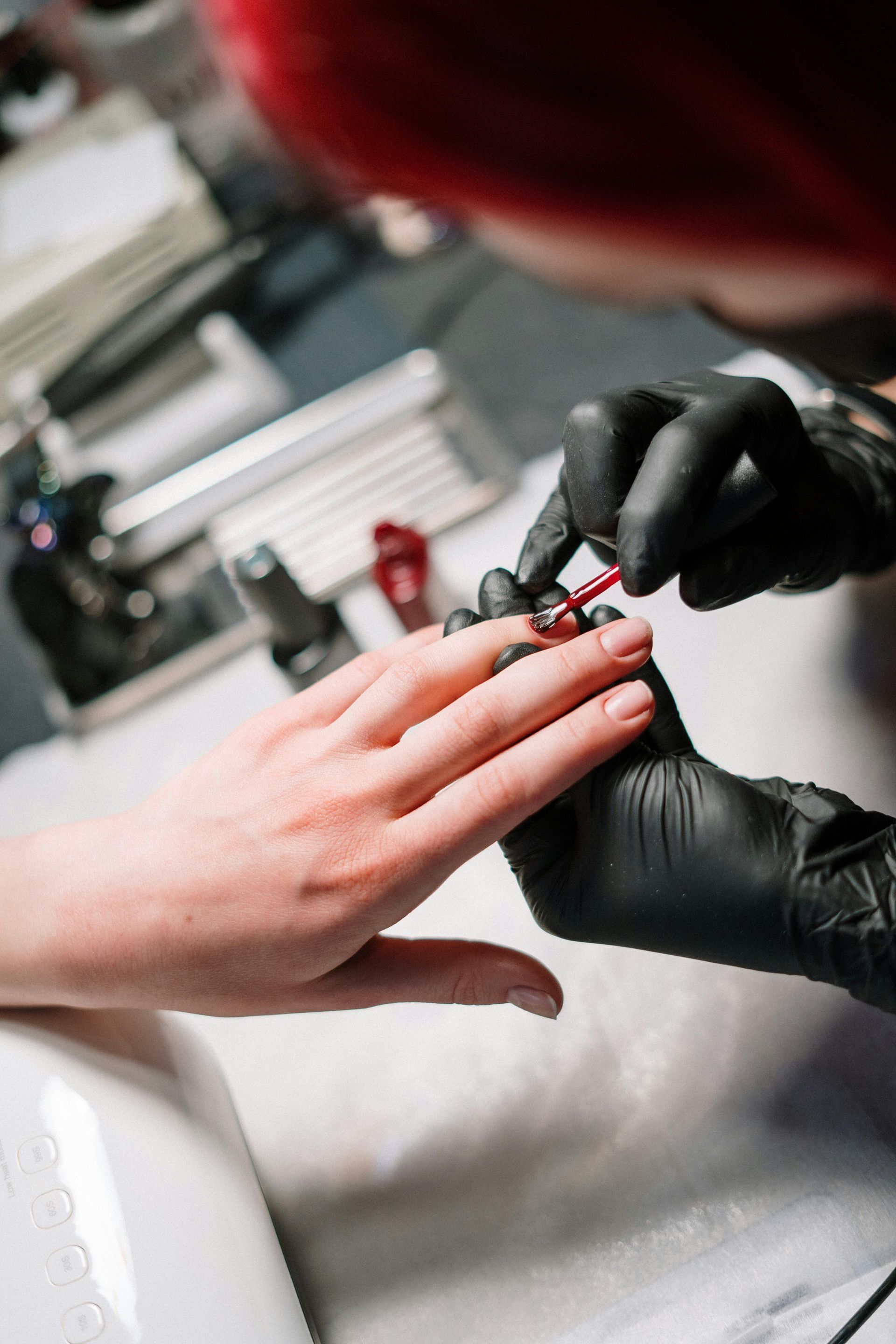 Nail technician painting a fingernail with red polish while wearing black gloves