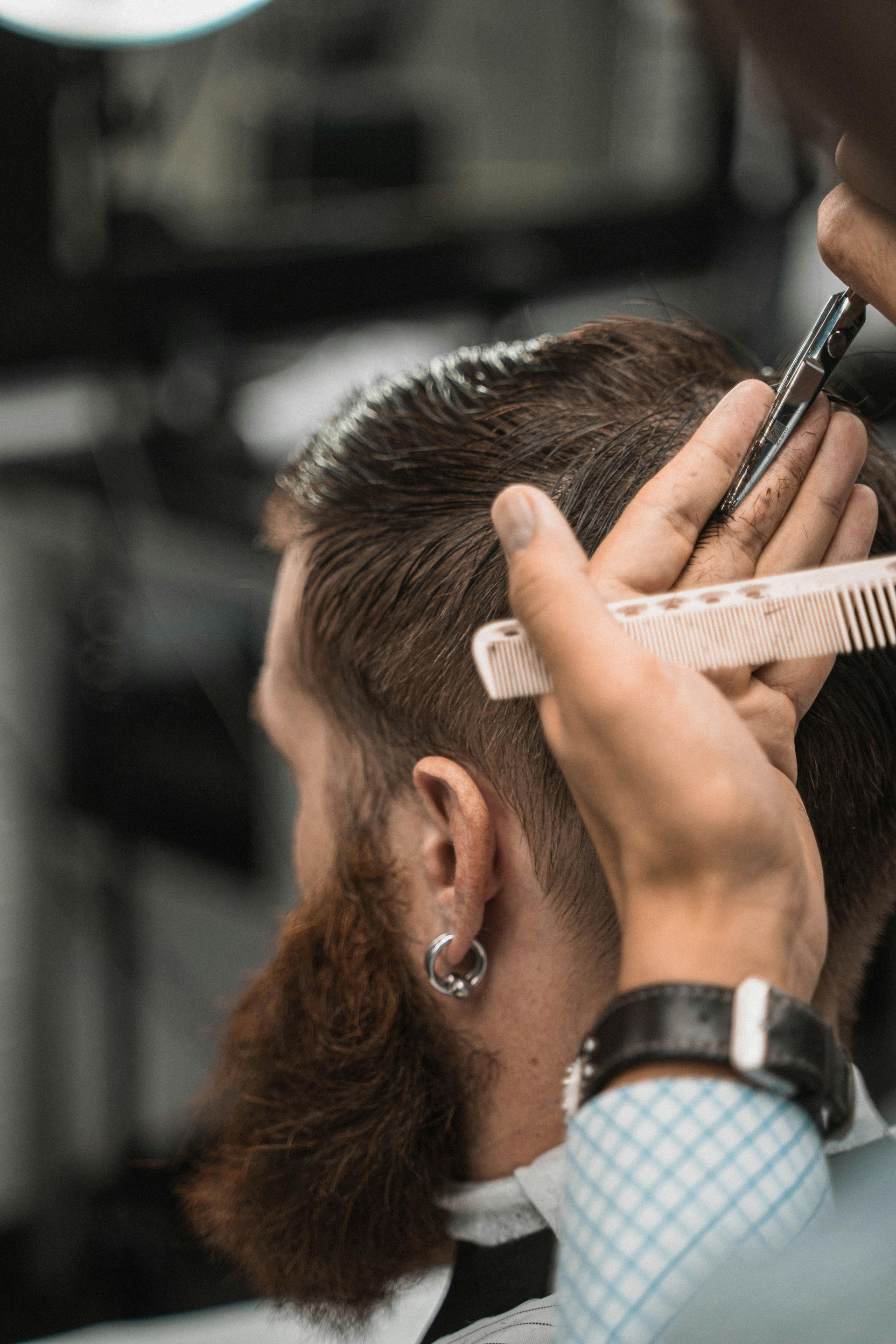 Hairdresser cutting wet, dark hair with scissors and comb.