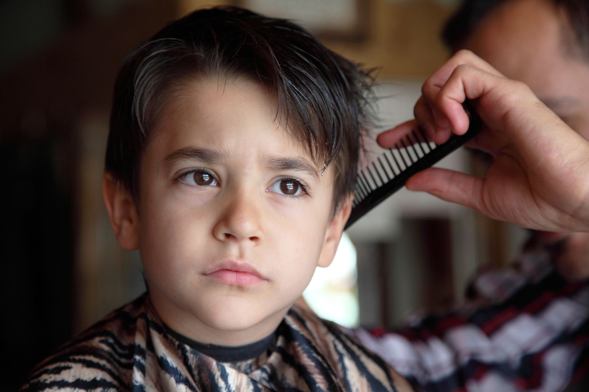 Child getting a haircut while a hand combs dark hair in a close-up scene