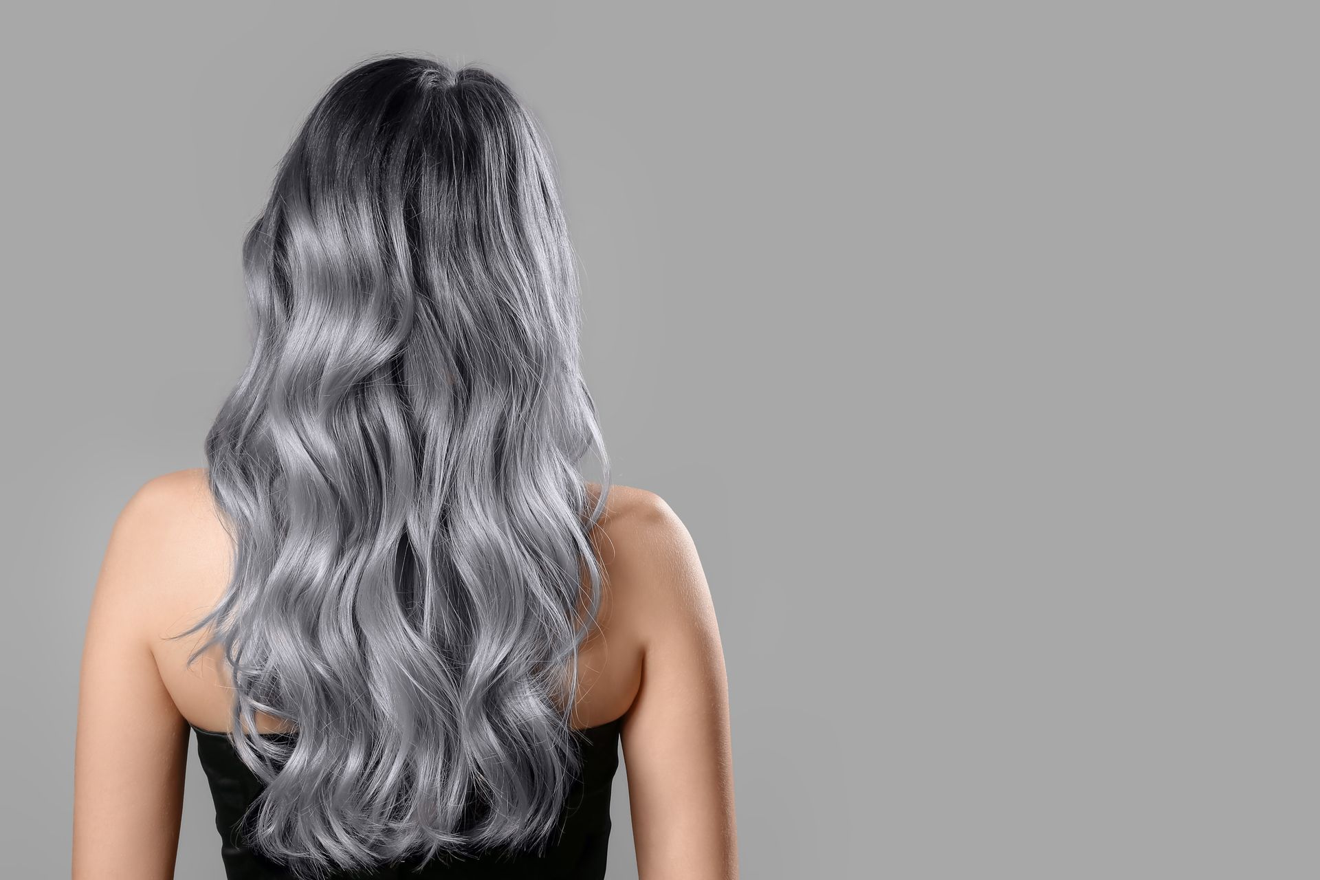 Back view of a person with long wavy silver hair against a gray background