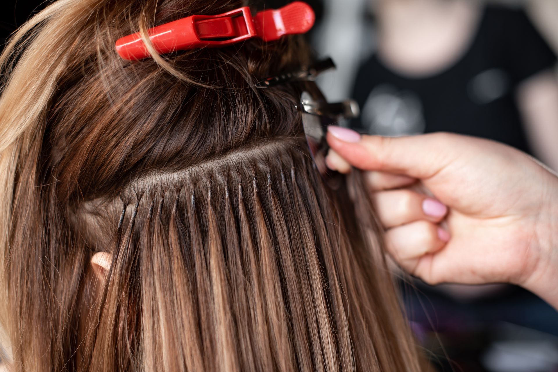 Hair being sectioned with a red clip while a hand braids or weaves strands in close-up.