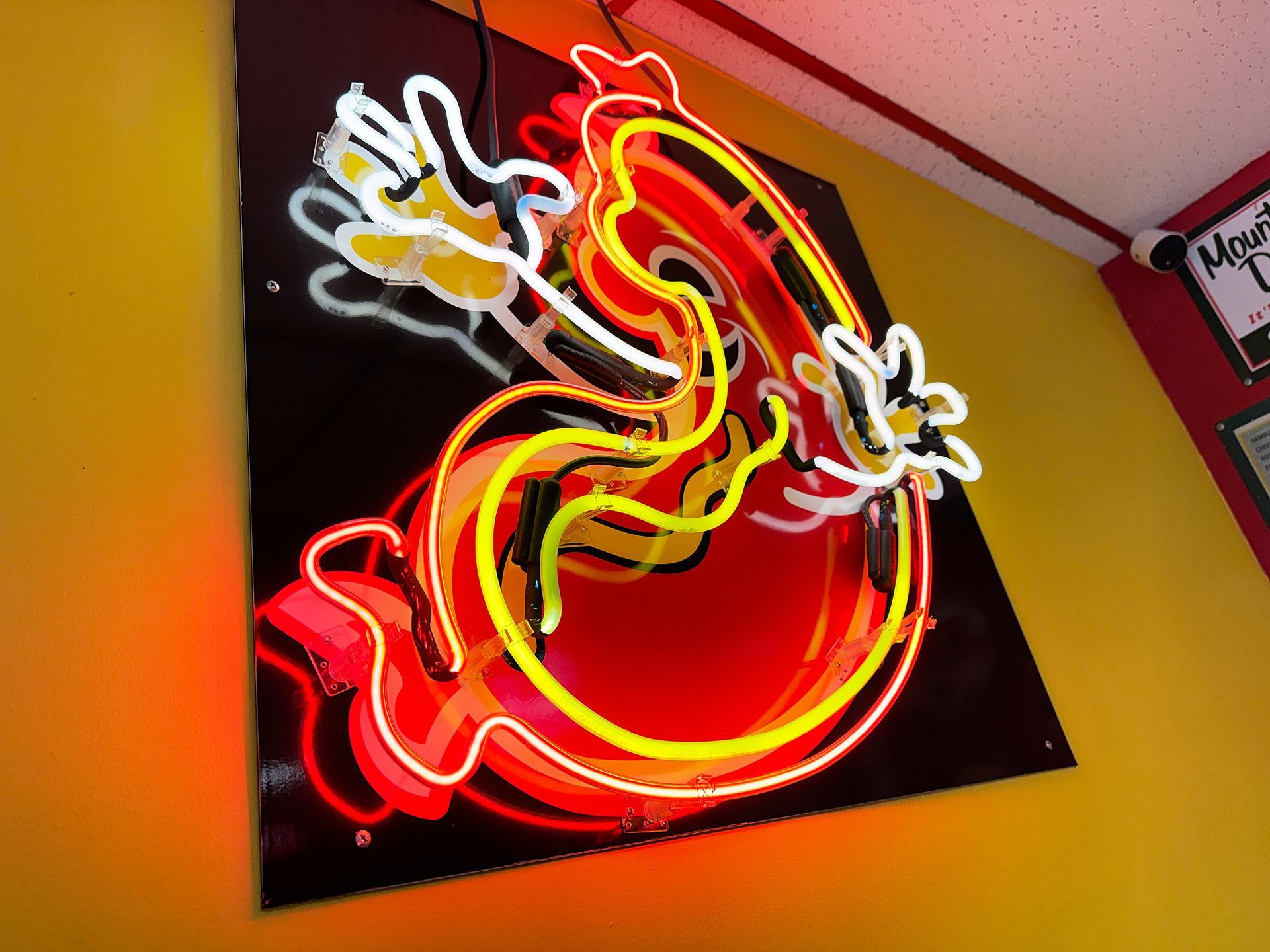 Neon sign of a stylized ghost with red, yellow, and white outlines on a black background, mounted on a yellow wall.