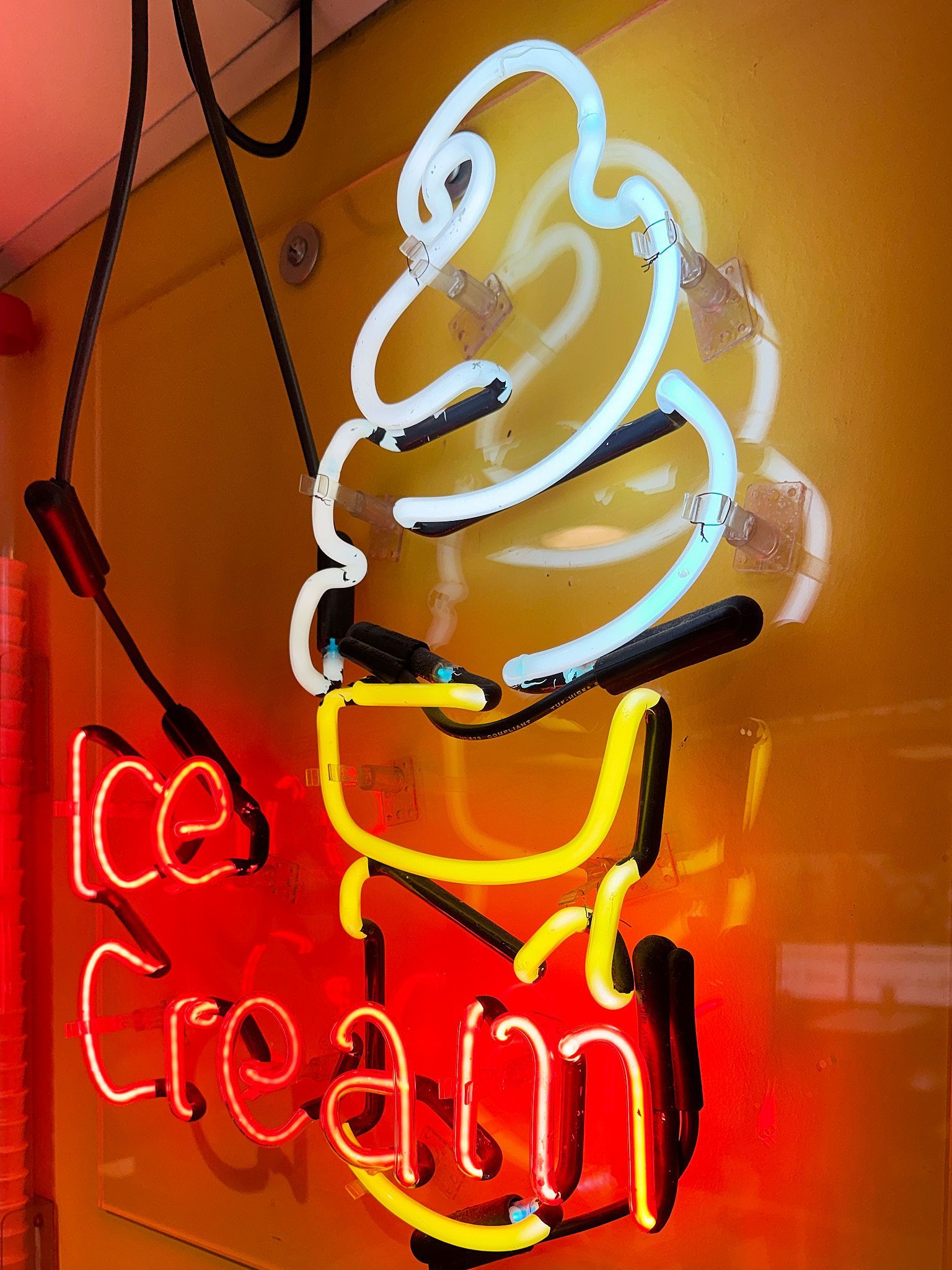 Neon ice cream cone sign on a yellow wall with the words 