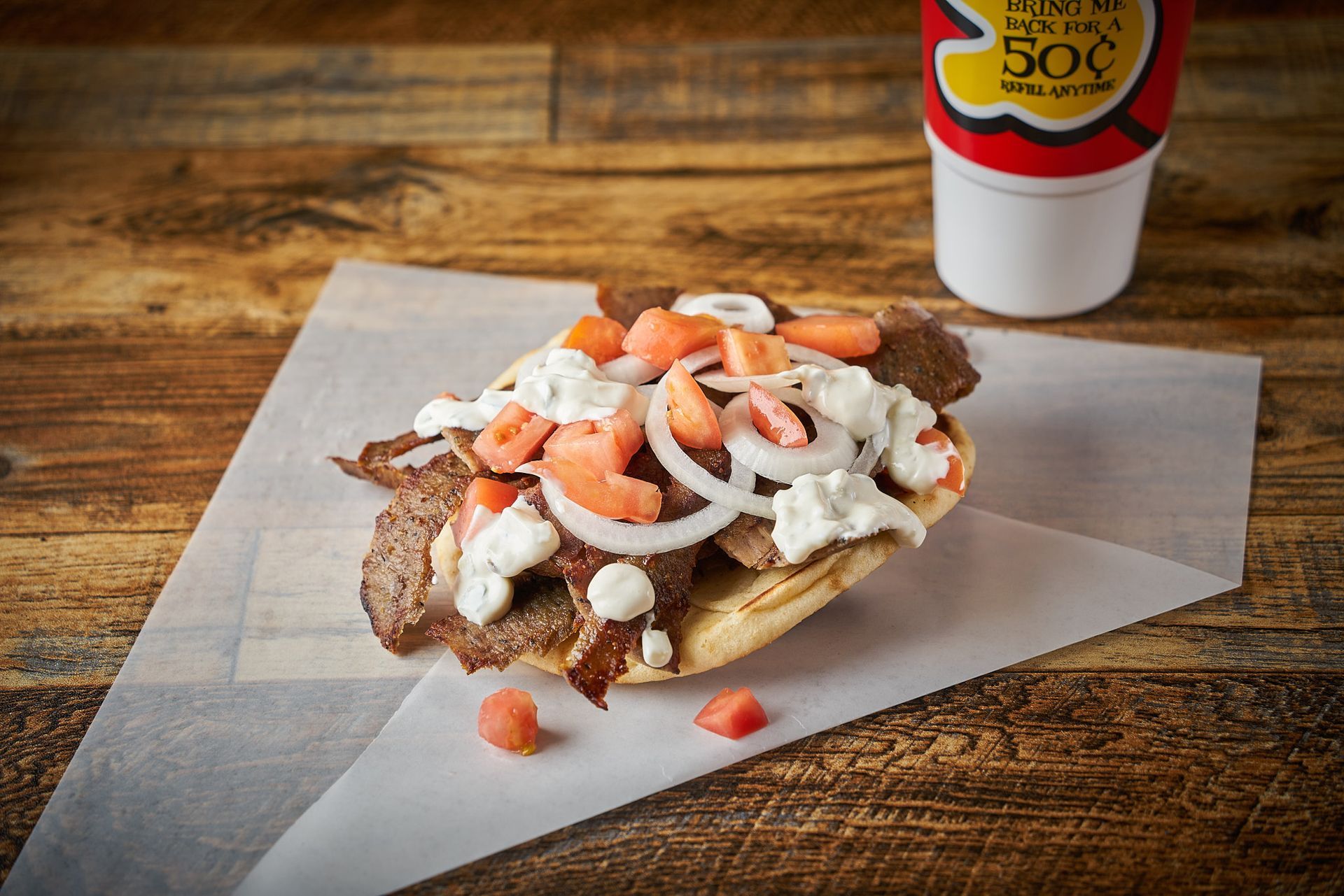 Gyro sandwich with meat, onions, and tomato on parchment paper; drink cup.