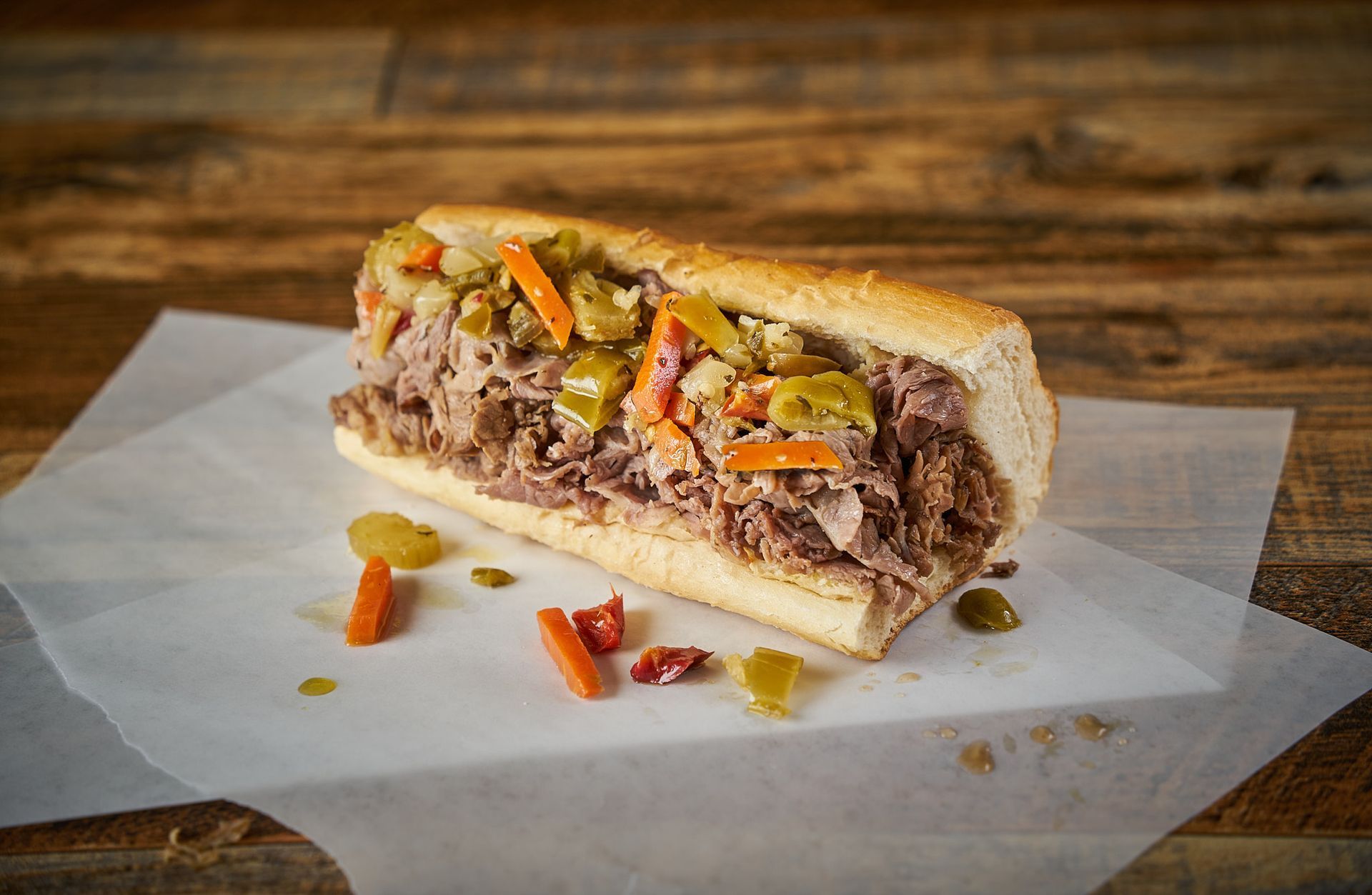 A long, bread-covered sandwich filled with meat, topped with relish, on a sheet of parchment paper.