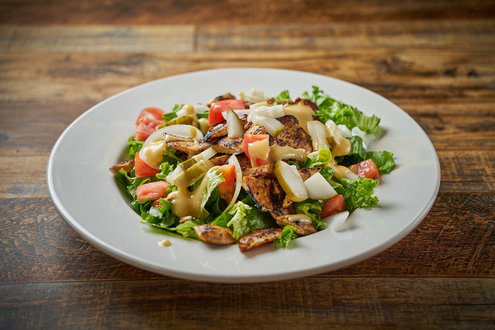 Salad with chicken, tomatoes, and pears on a white plate, wooden table.