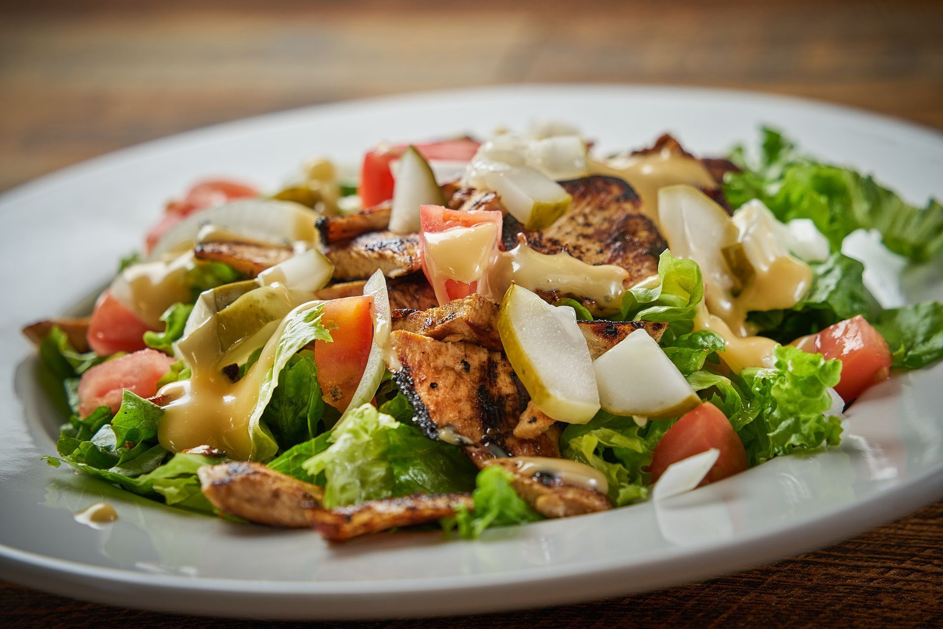 Salad with lettuce, tomatoes, grilled chicken, pears, and dressing on a white plate.
