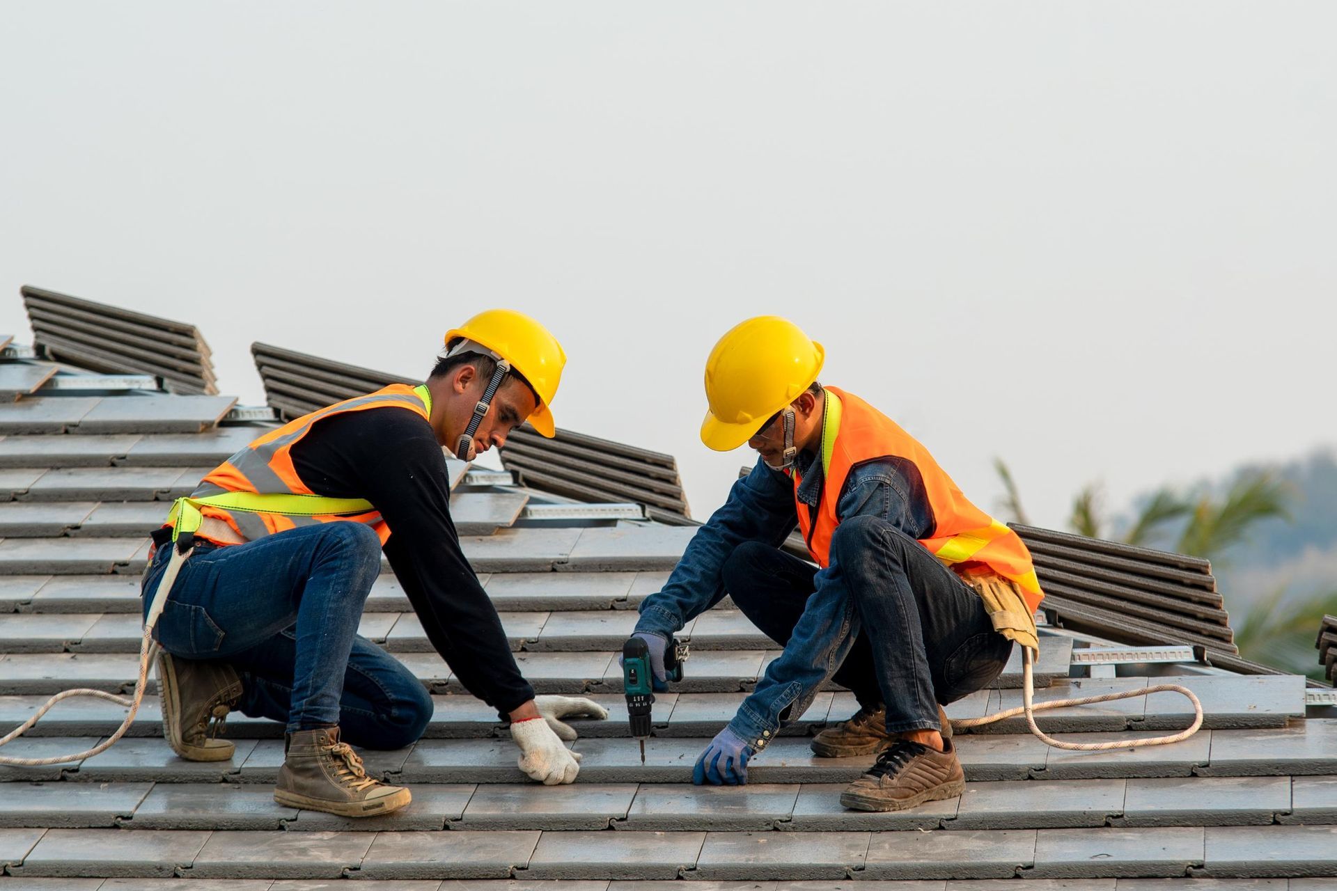 Two roofers in yellow hard hats installing metal roofing on a house rooftop