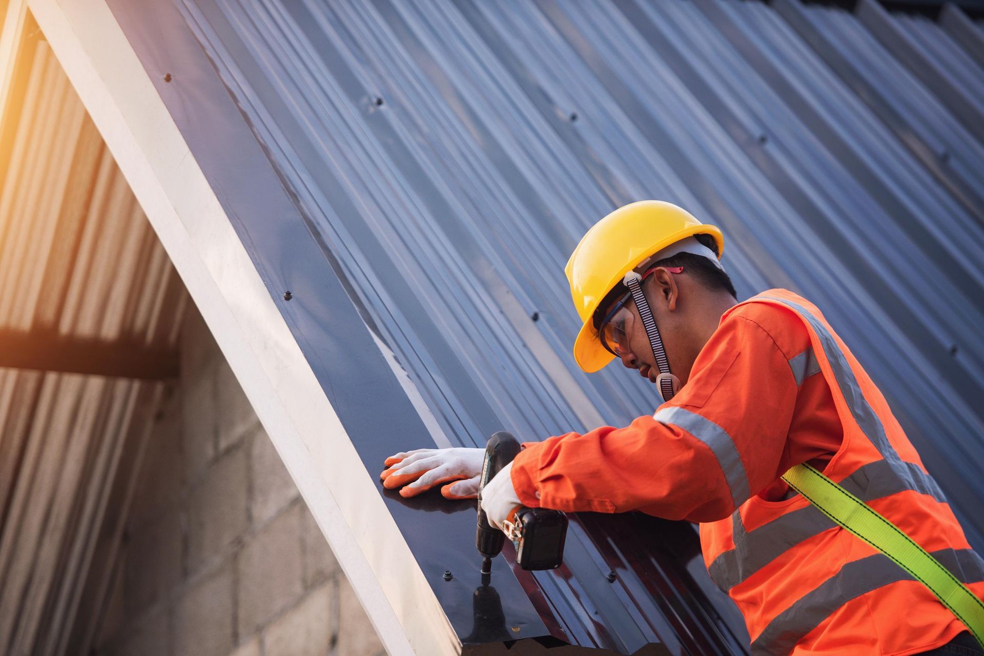 Worker in a yellow hard hat installing a dark metal roof panel on a building.