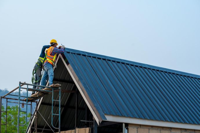 Worker on scaffolding installing a blue metal roof on a house under construction