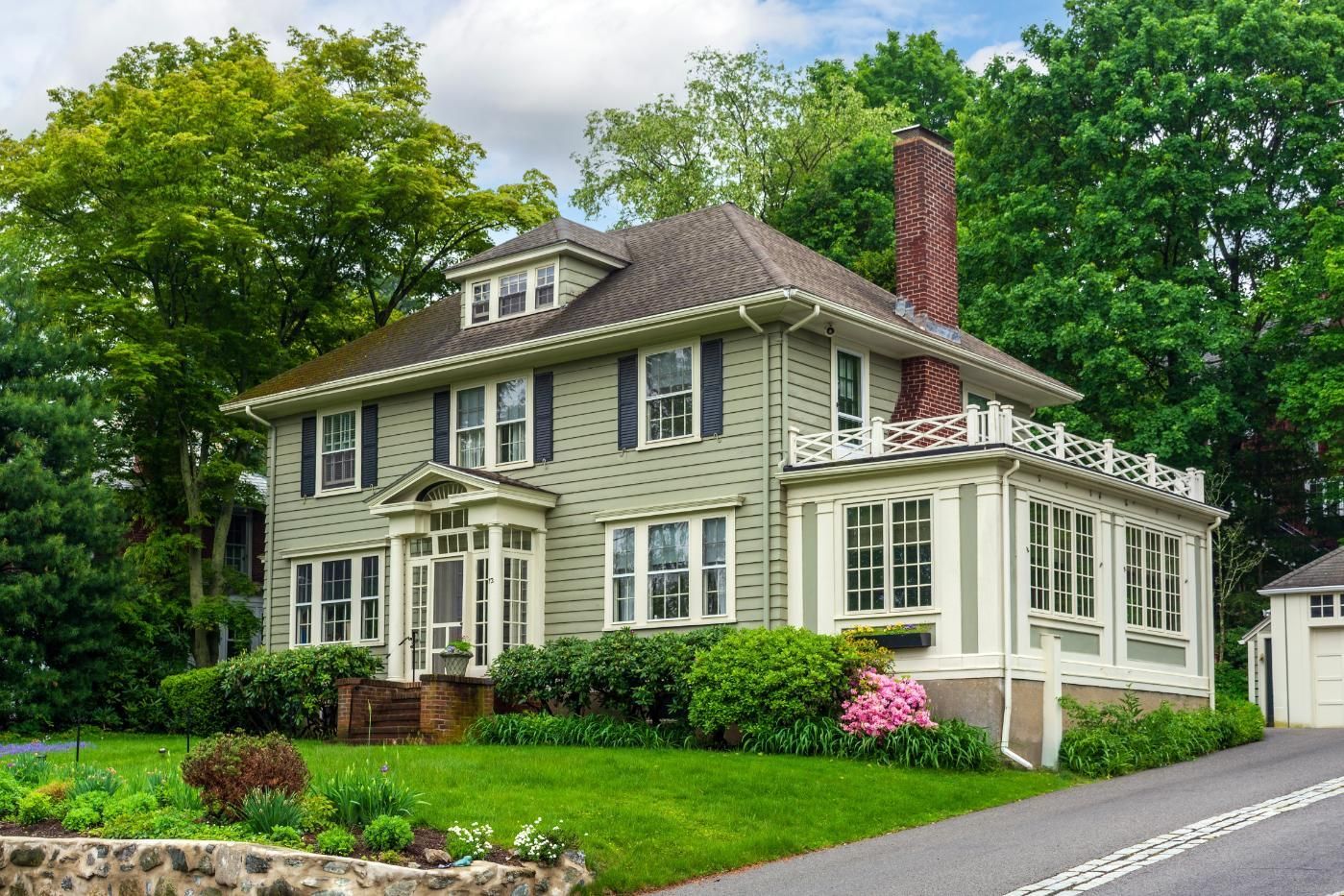 Two-story beige house with white trim, red chimney, and lush green trees and lawn