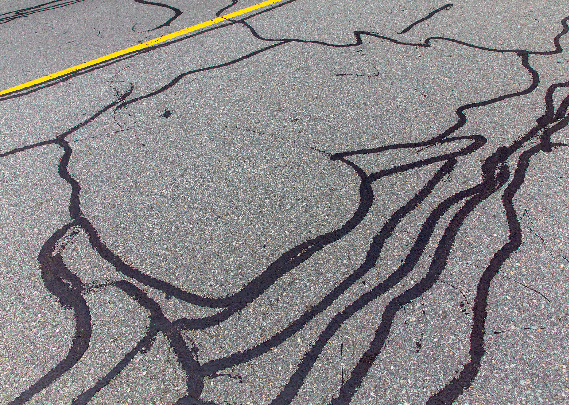 Black asphalt with cracks filled in black; yellow line in the corner.