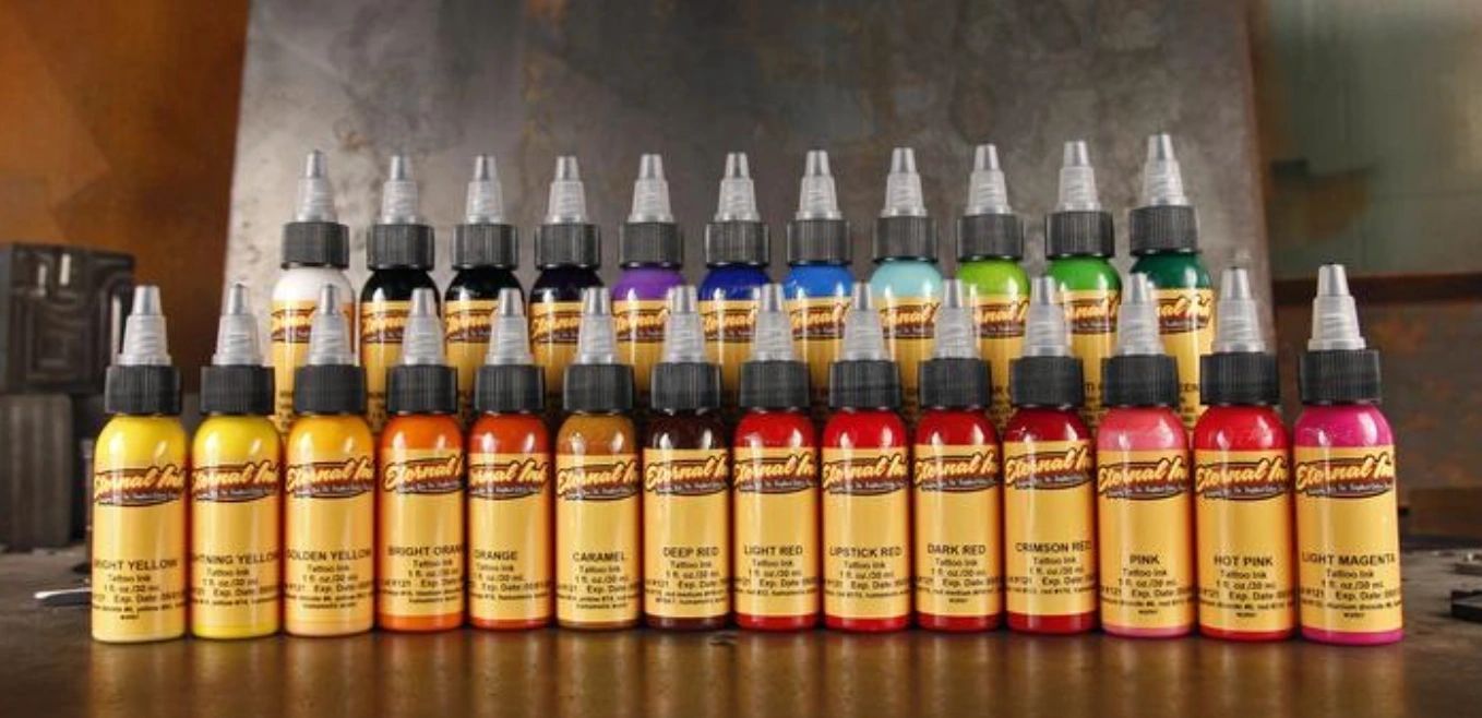 A row of bottles of tattoo ink are lined up on a table.