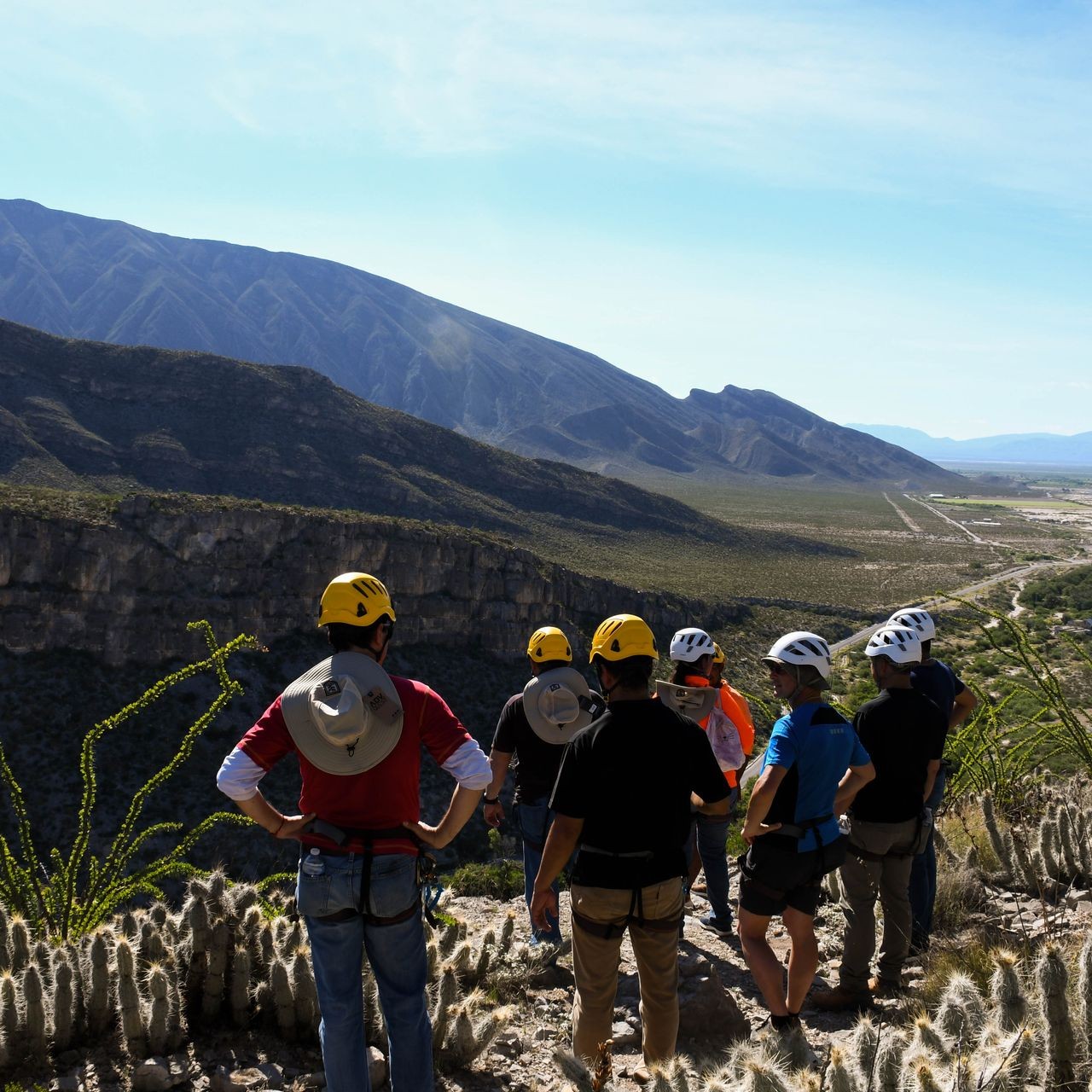 Grupo de personas con cascos con vistas a un cañón, montañas al fondo, día soleado.
