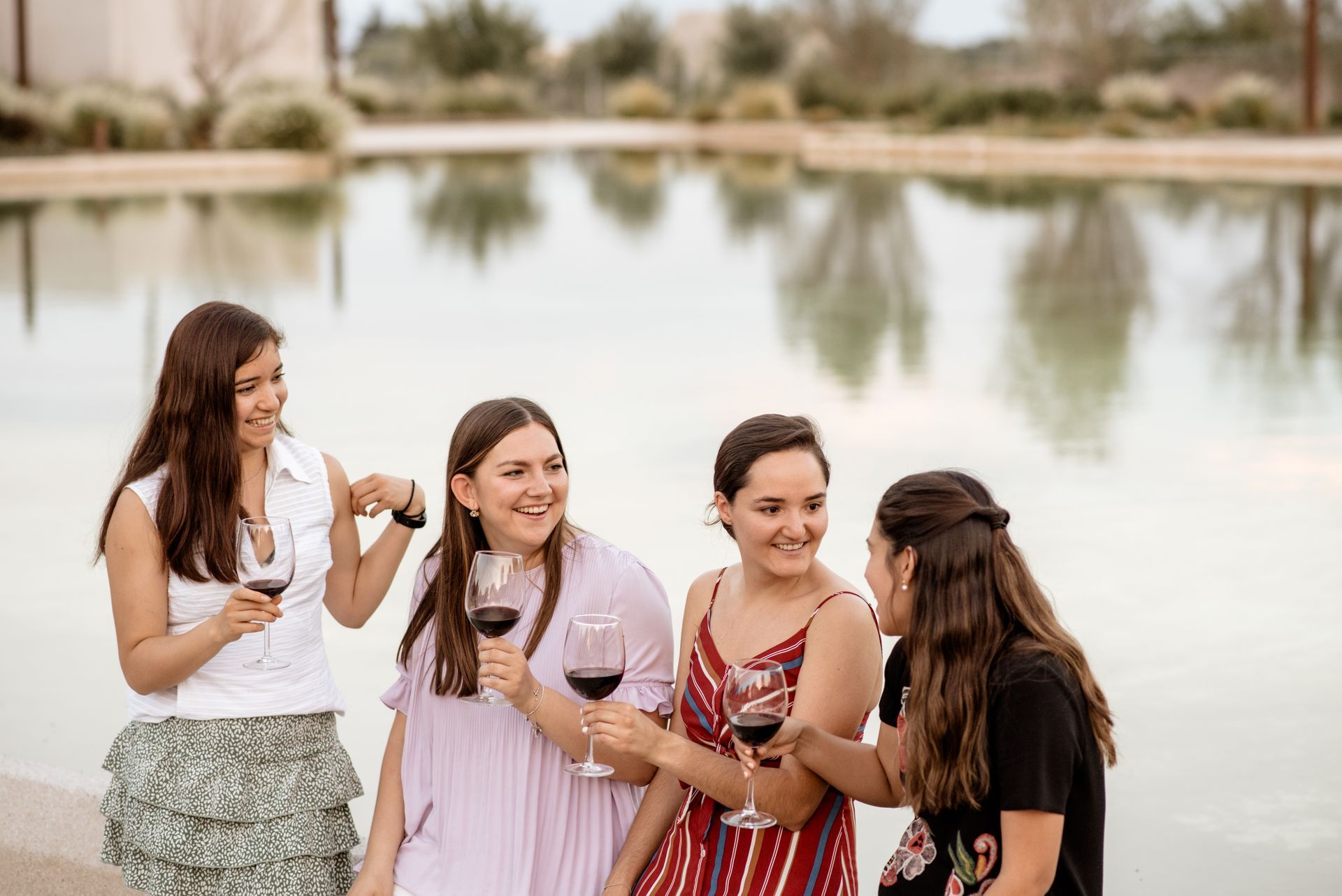 Un grupo de mujeres brinda con copas de vino frente a un lago.