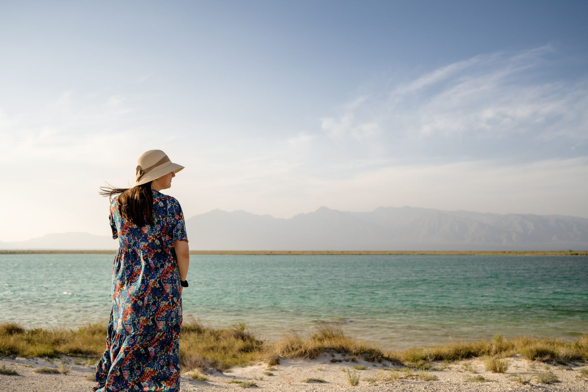Una mujer con vestido y sombrero está parada en una playa mirando el océano.