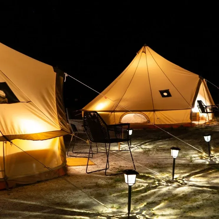 Dos tiendas de lona iluminadas por la noche, con luces en el camino que conducen hasta ellas.