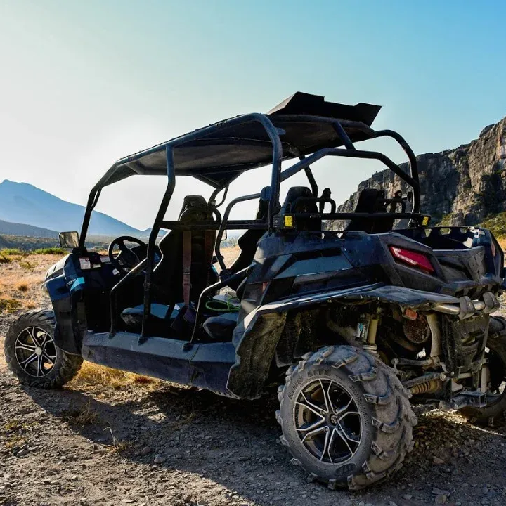 Vehículo todoterreno azul oscuro en un camino de tierra con montañas al fondo bajo un cielo azul.