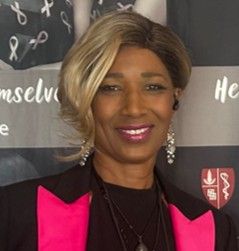 A person smiling, wearing a black blazer with bright pink lapels, in front of a banner with medical and ribbon graphics.