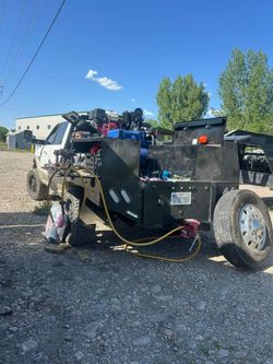 A black utility truck with equipment and tools parked on gravel under a blue sky.  A white building is visible in the background.