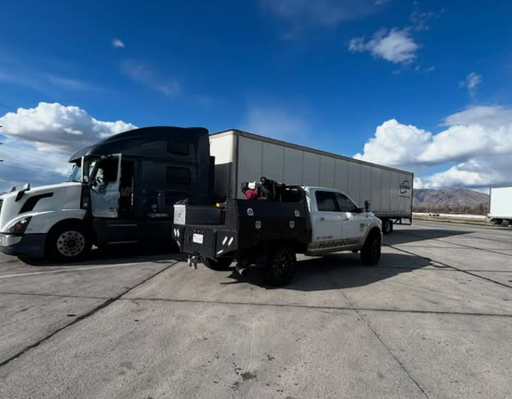 A semi-truck and a pickup truck parked next to a trailer on a paved lot under a blue sky.