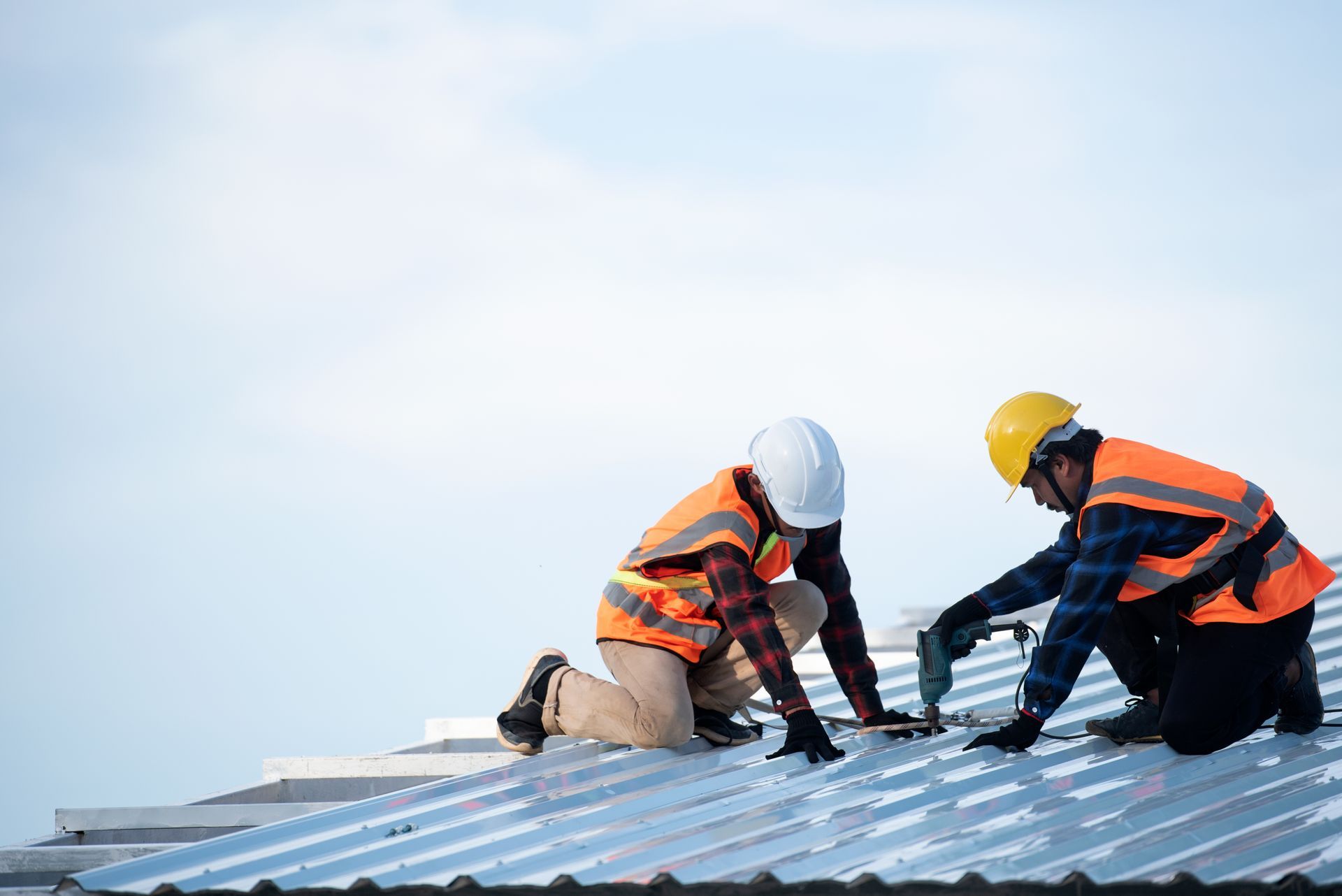 Two workers in hard hats install roofing panels on a rooftop under a cloudy sky