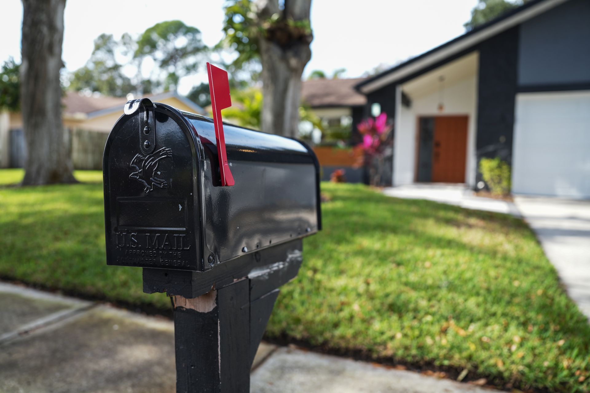 Black mailbox with a red flag by a suburban driveway and house.