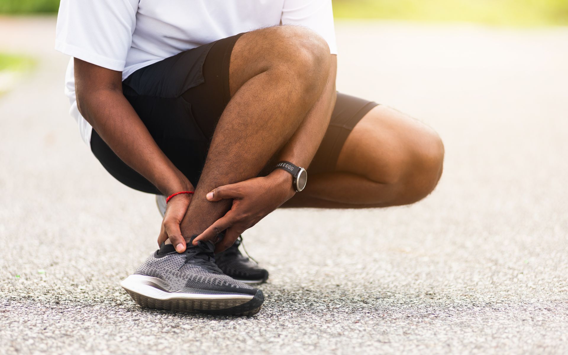 Man crouching, holding his ankle in pain on a gravel path, wearing athletic clothes.