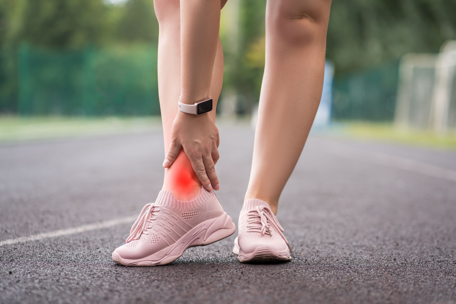 Woman holding ankle in pain on a running track, red highlight indicating injury.