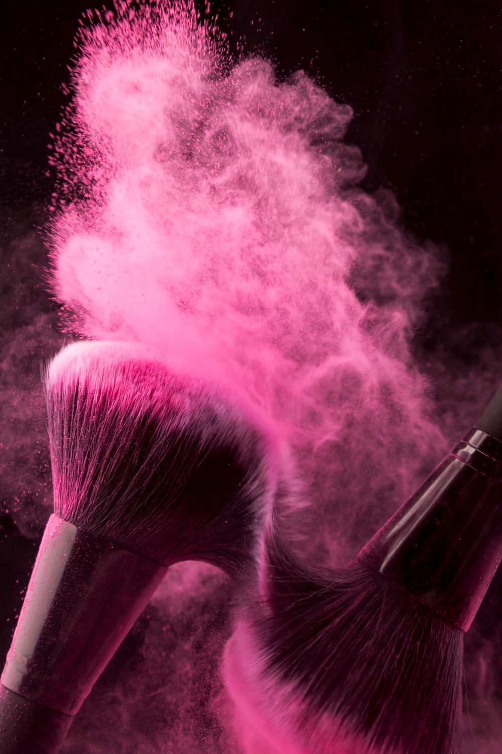 A close up of a makeup brush with pink powder coming out of it.