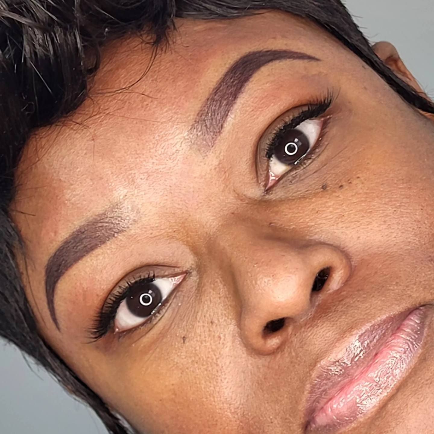 Close-up of a person’s face showing curled lashes with eyeliner, neatly shaped eyebrows and glossy lips