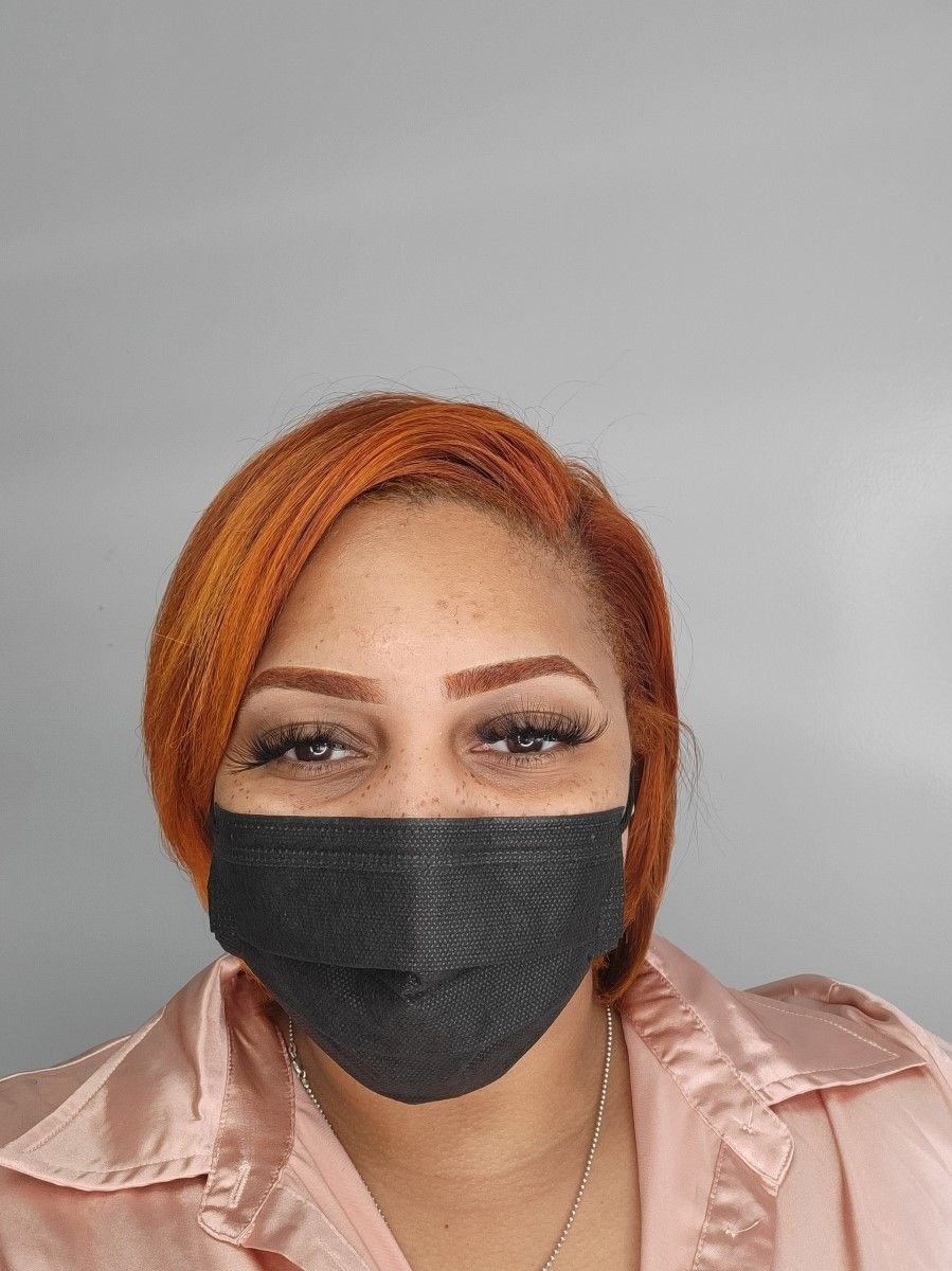 a woman with orange hair, bold brows, long eyelash extensions, freckles, and a black face mask.