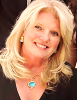 Smiling person with shoulder-length blonde hair wearing a turquoise pendant necklace and matching earrings.