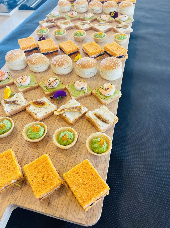 Planche en bois avec assortiment d'entrées : sandwichs, tartes et bouchées, prêtes à servir.