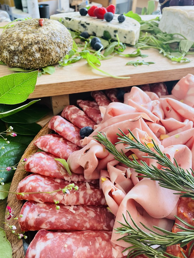 Planche de charcuterie avec charcuteries, fromages et baies, avec herbes et légumes verts.