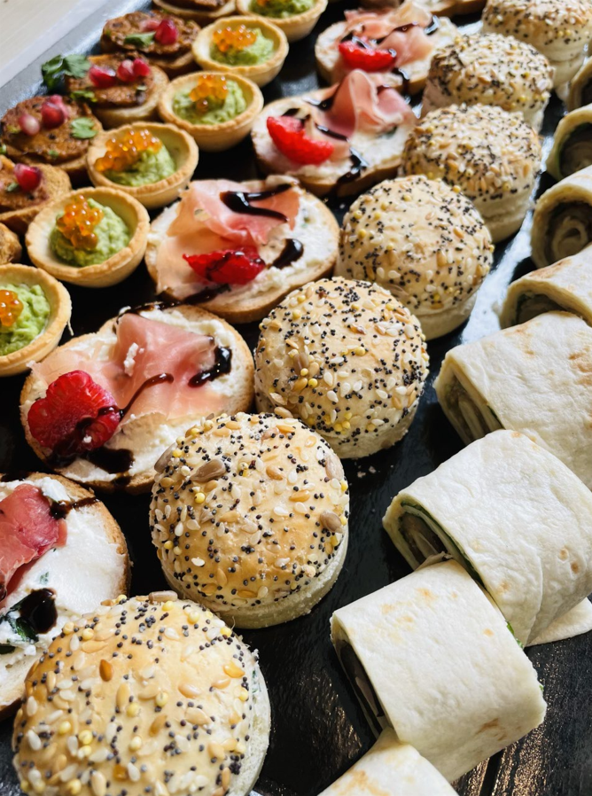 Gros plan d'un plateau avec divers hors-d'œuvre : tartes, petits pains aux graines et tortillas roulées.