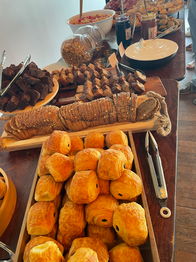 Une table chargée de pâtisseries variées, de pain, de brownies et de confitures pour un buffet brunch.