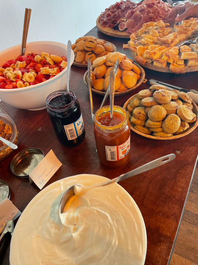 Petit déjeuner buffet avec fruits, viennoiseries, confitures, yaourts et charcuterie sur une table en bois.