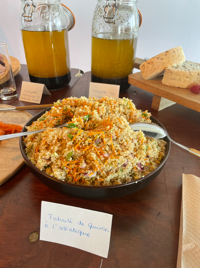 Salade de quinoa avec légumes, pain et huile infusée sur une table en bois.