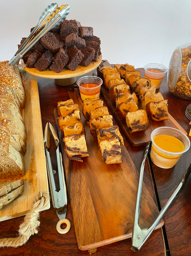 Une table présente des brownies, du pain et d'autres desserts avec des sauces et des pinces de service.