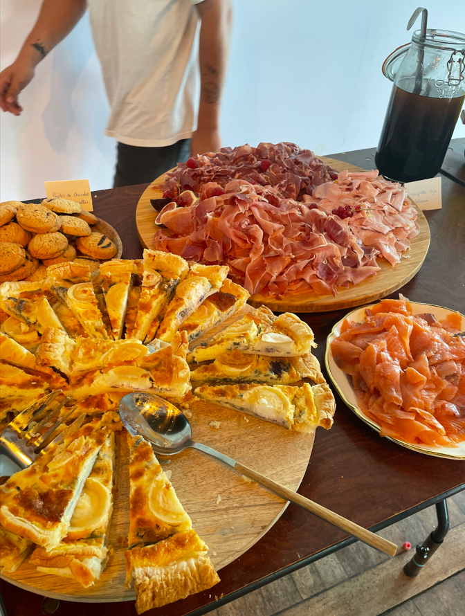 Un buffet avec quiches, biscuits, charcuterie et saumon. Une personne se tient à proximité.