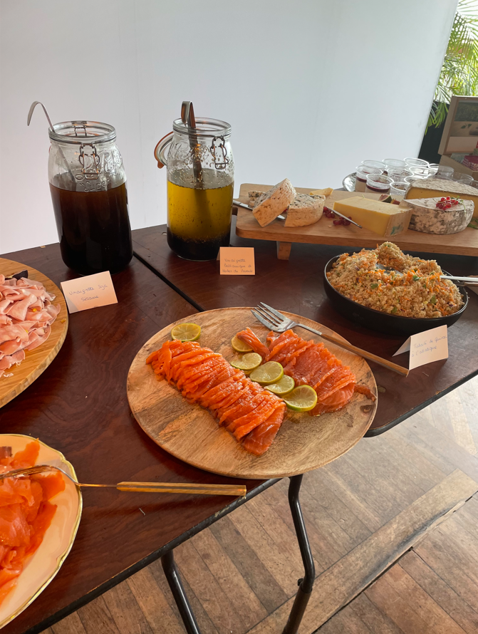 Buffet avec saumon fumé, fromage, céréales et vinaigrettes sur une table en bois.