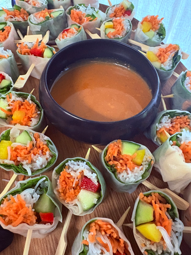Rouleaux de printemps sur des brochettes autour d'un bol de sauce à tremper sur une planche en bois.