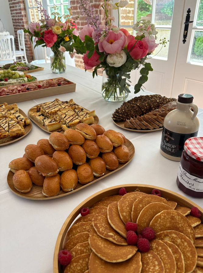 Une table de buffet avec des pâtisseries, des crêpes et des fleurs disposées pour un repas.
