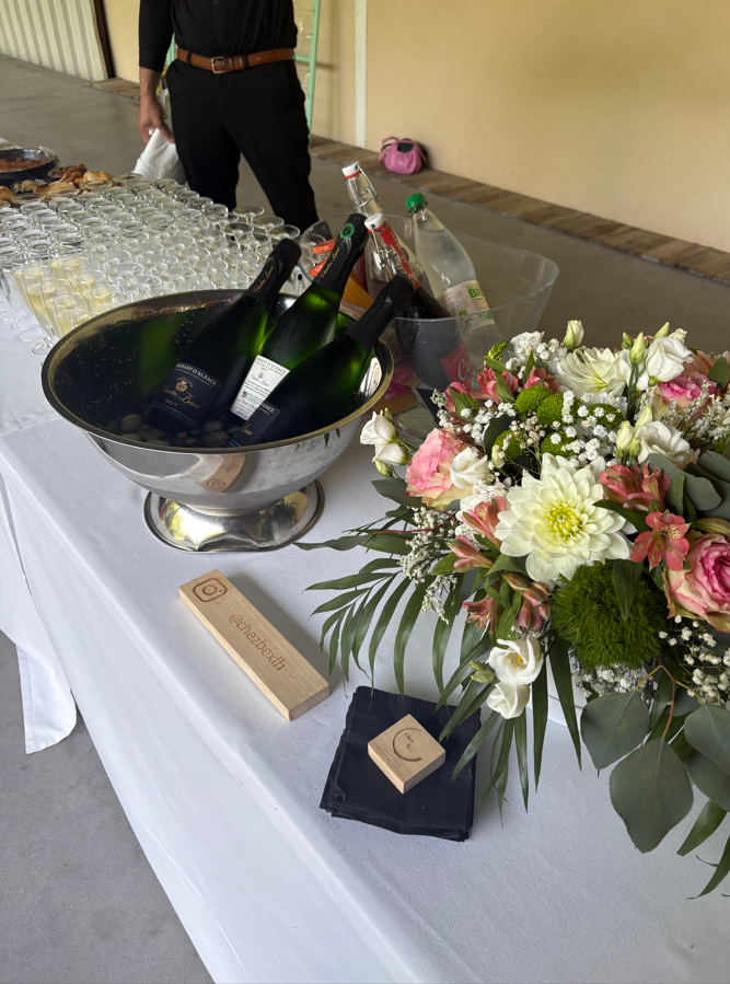 Bouteilles de champagne dans un seau à glace, verres, fleurs et objets en bois sur une table.