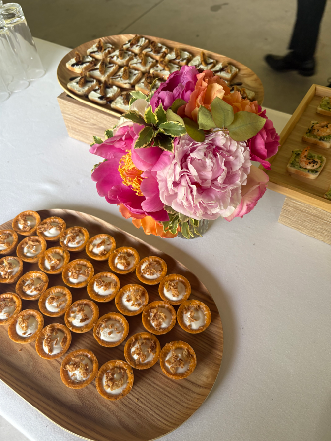 Apéritifs sur des plateaux en bois avec un centre de table floral sur une nappe blanche.