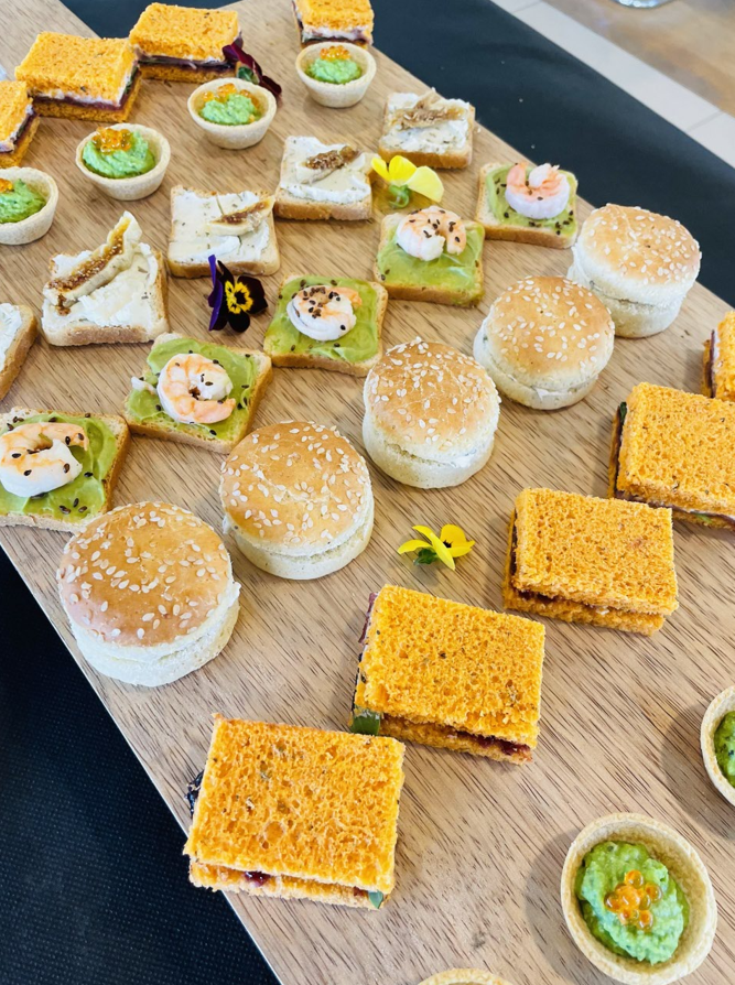 Planche en bois avec assortiment d'amuse-gueules : mini sandwichs, toasts à l'avocat et tartelettes.