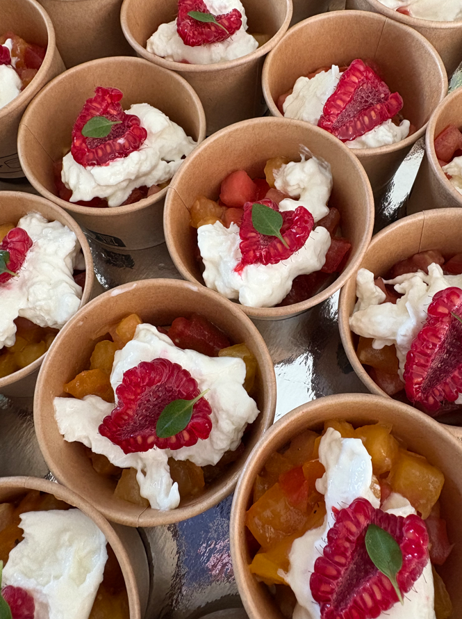 Parfaits de salade de fruits dans de petites coupes brunes, garnis de crème fouettée, de framboises et de menthe.