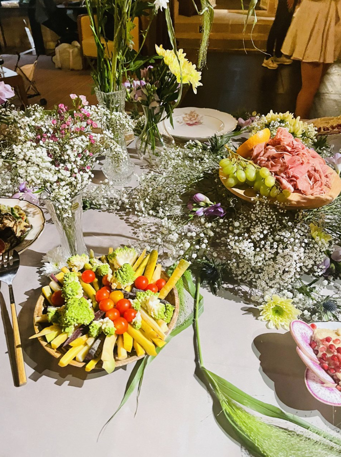 Table avec fleurs, légumes et fruits. Une personne se tient à proximité.